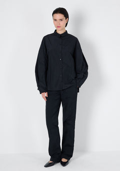 Schwarze Bluse mit einem Blusenkragen und einer kurzen Passform. Die Ärmel sind überschnitten und haben voluminöse Falten.